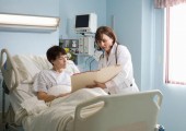 Doctor showing medical chart to patient who is lying in hospital bed