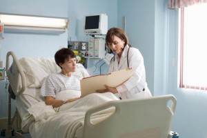 Doctor showing medical chart to patient who is lying in hospital bed